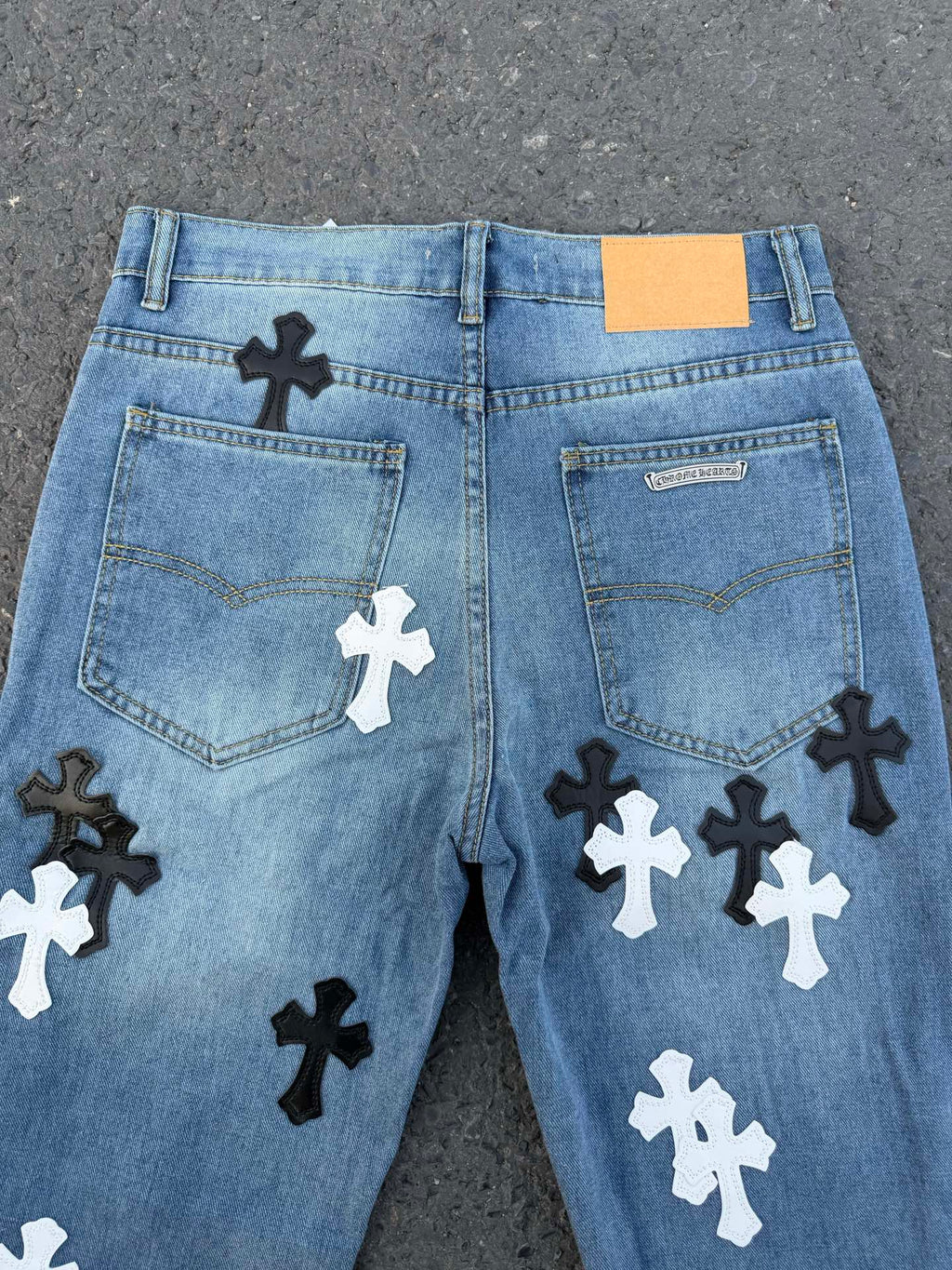 Back view of light blue denim pants with multiple black and white cross patches