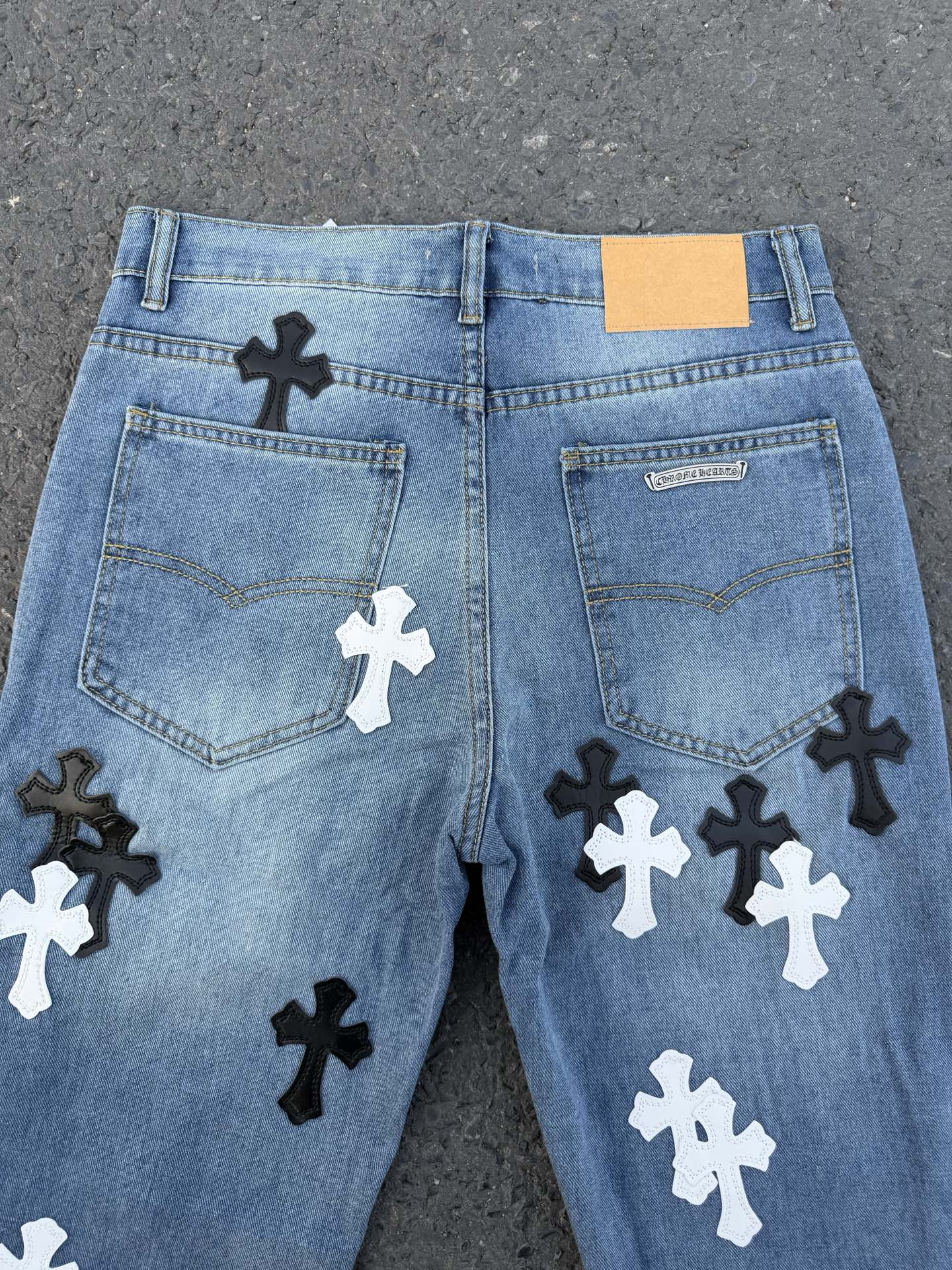 Back view of light blue denim pants with multiple black and white cross patches