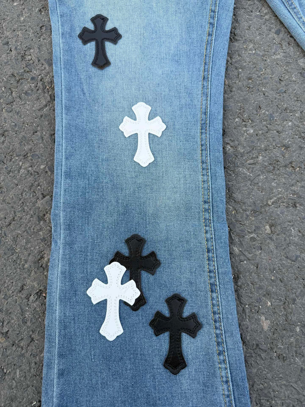 Close-up of light blue denim pants leg with black and white cross patches