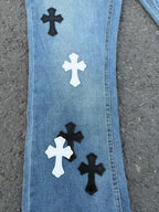 Close-up of light blue denim pants leg with black and white cross patches