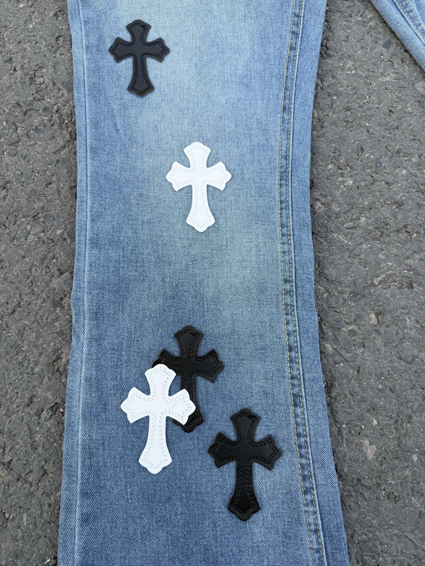 Close-up of light blue denim pants leg with black and white cross patches