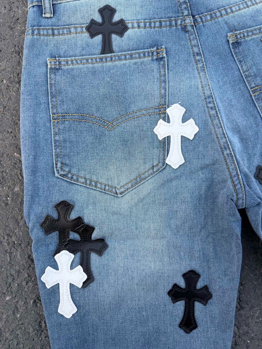 Close-up of back of light blue denim pants with heart pocket and cross patches