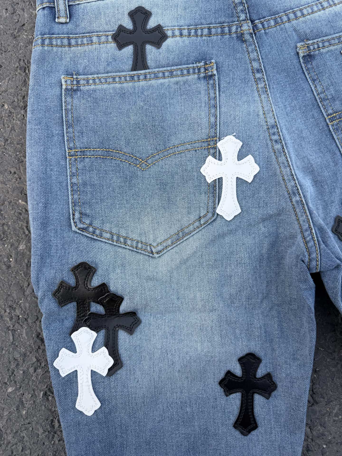 Close-up of back of light blue denim pants with heart pocket and cross patches