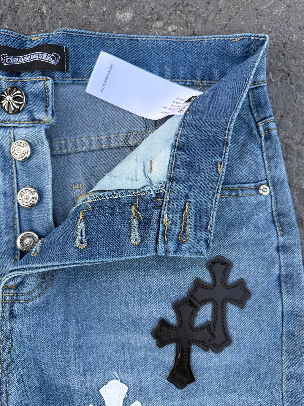 Close-up of light blue denim pants with cross patch and metal button details