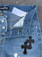 Close-up of light blue denim pants with cross patch and metal button details