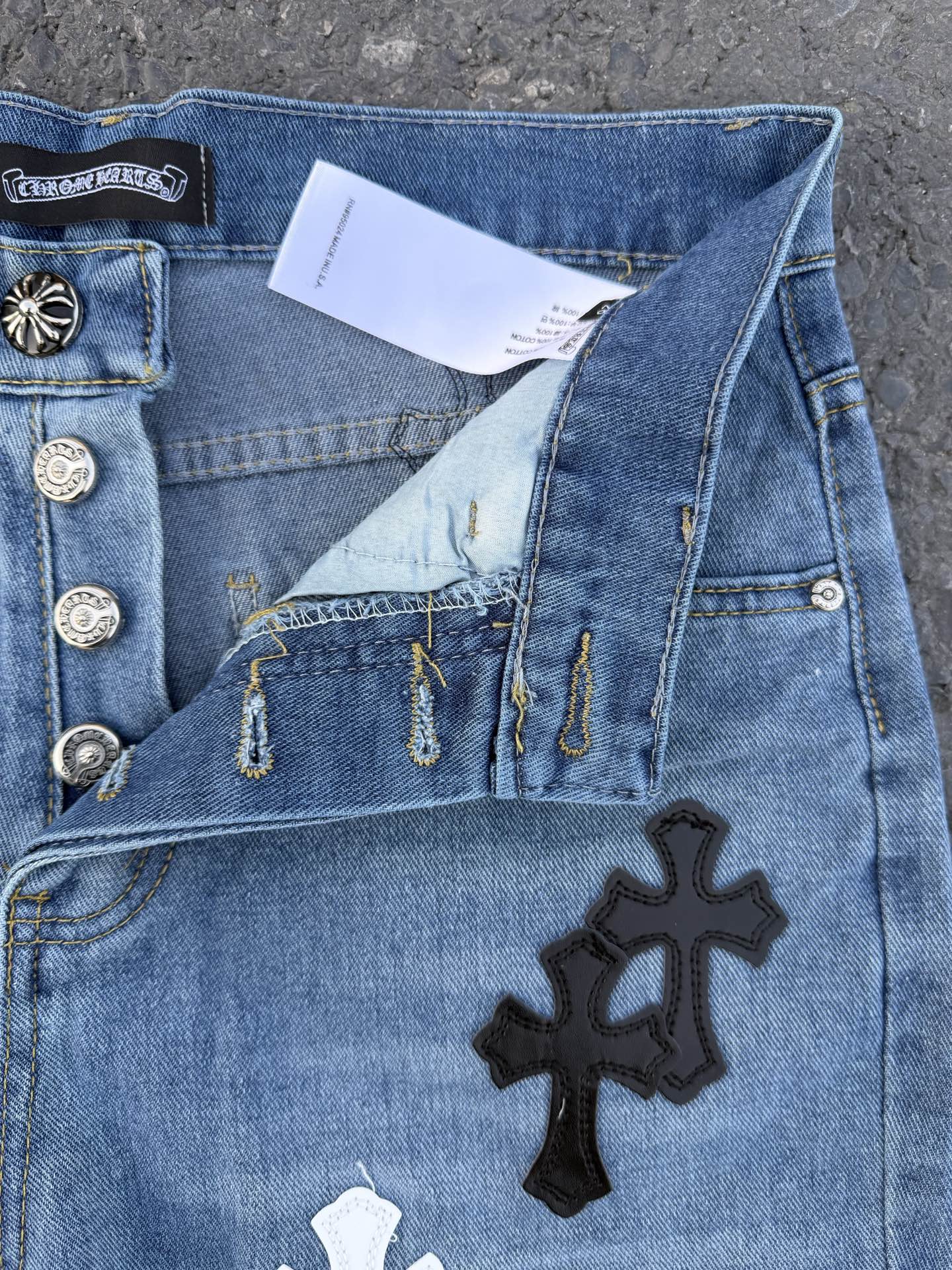 Close-up of light blue denim pants with cross patch and metal button details