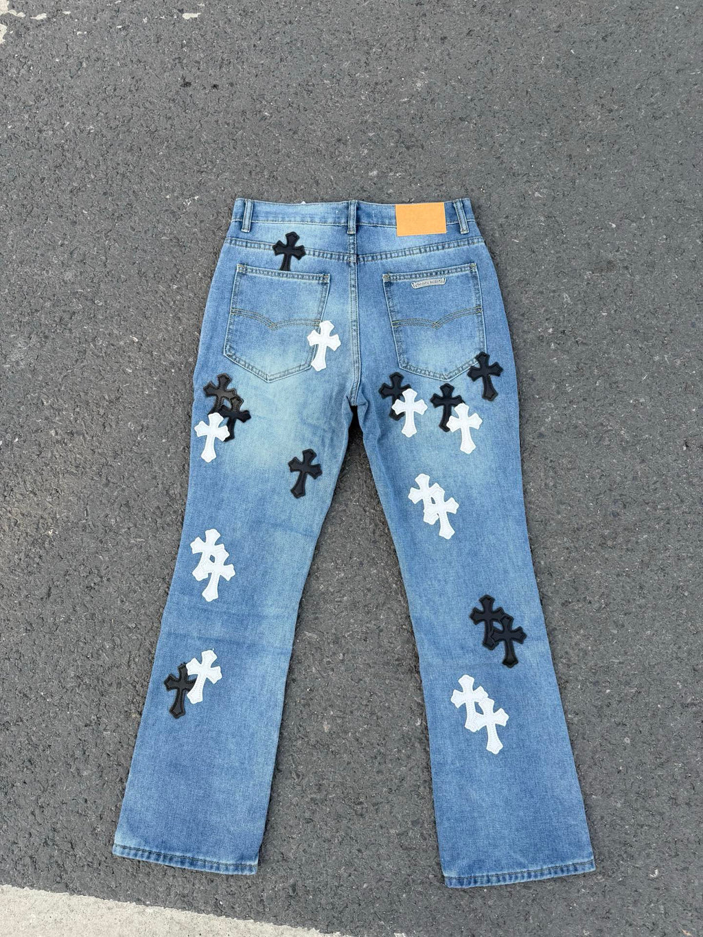 Light blue denim pants featuring scattered black and white cross patches
