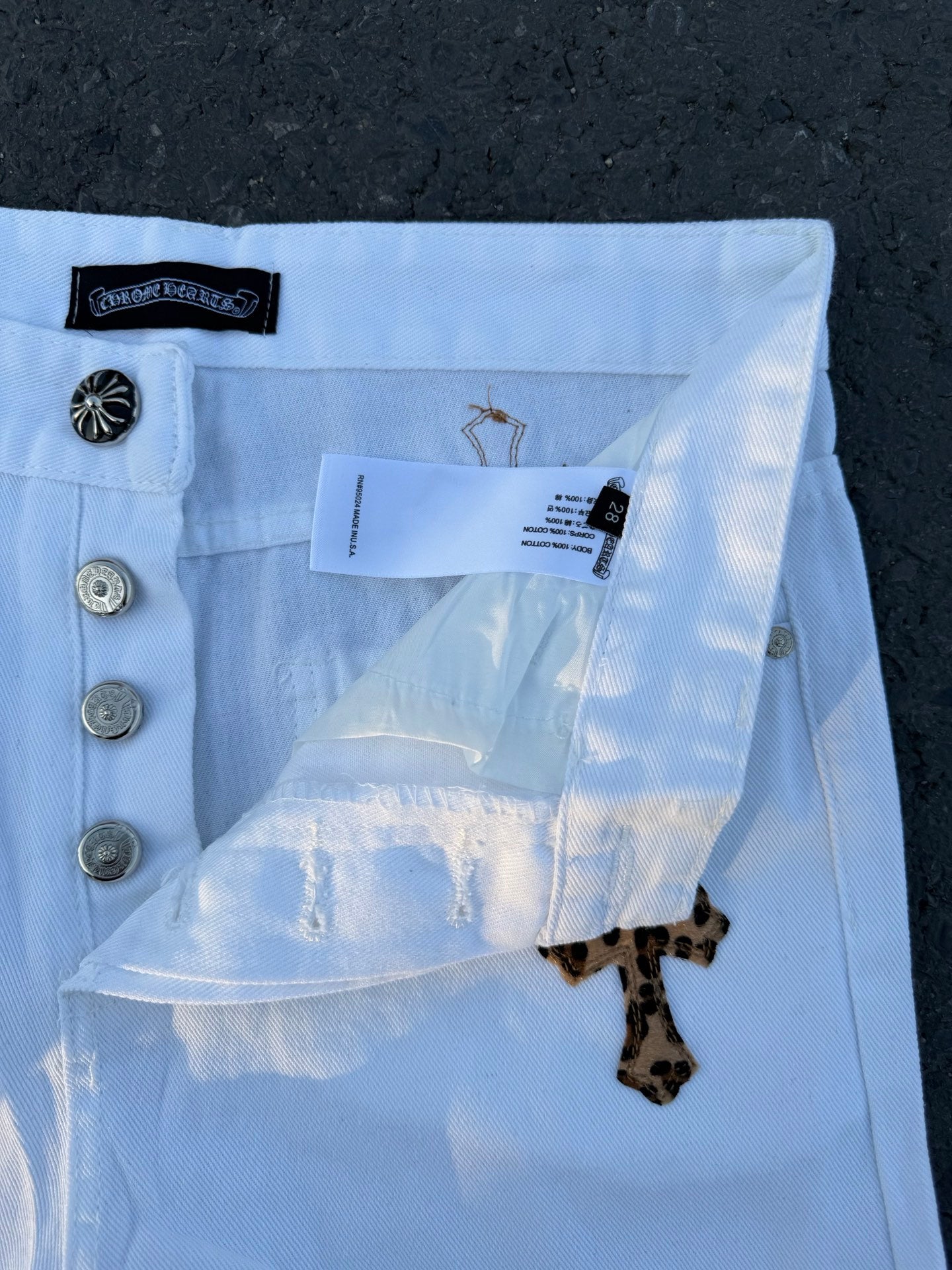 Light blue pants with front coin pocket, button fly, and dark cross patch on leg