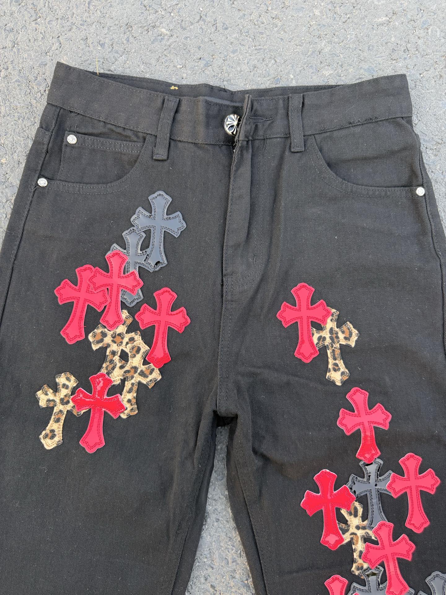 Dark gray denim pants with multicolor cross applique on the front panels.