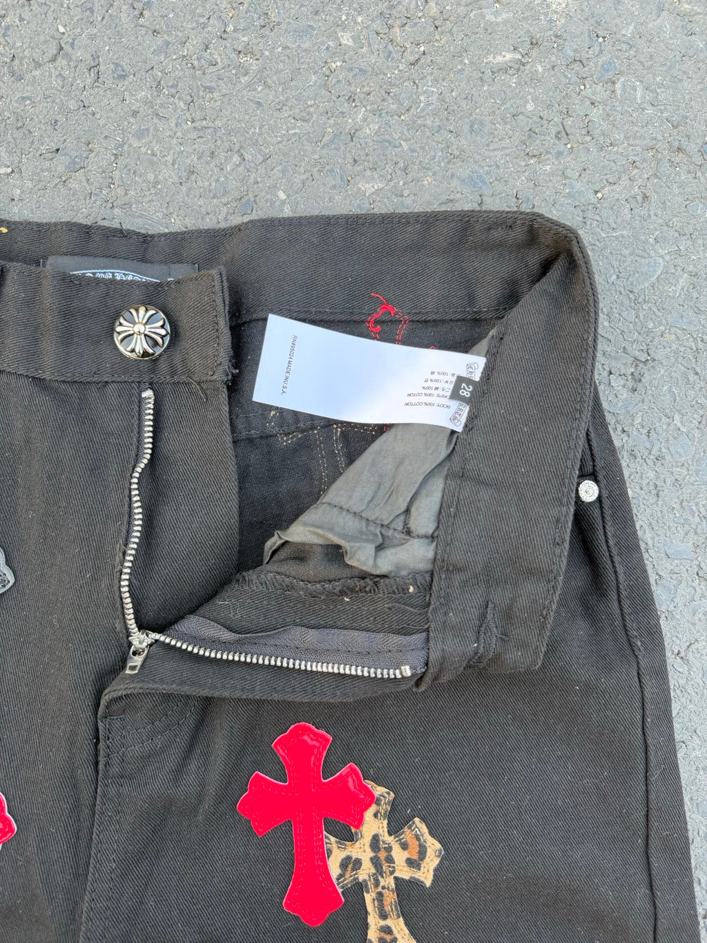 Dark gray denim pants with side zipper detail and cross applique on the leg.