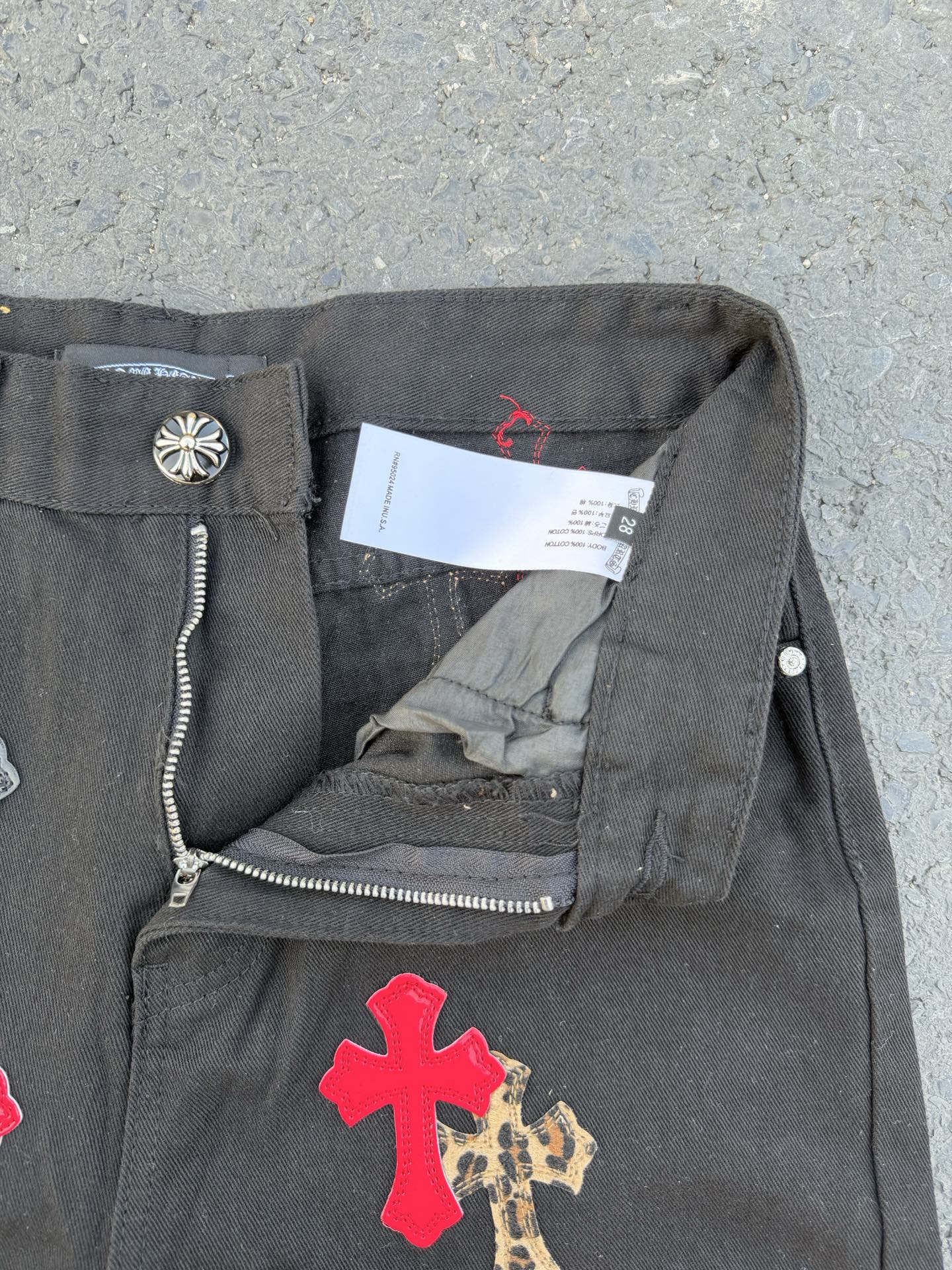 Dark gray denim pants with side zipper detail and cross applique on the leg.