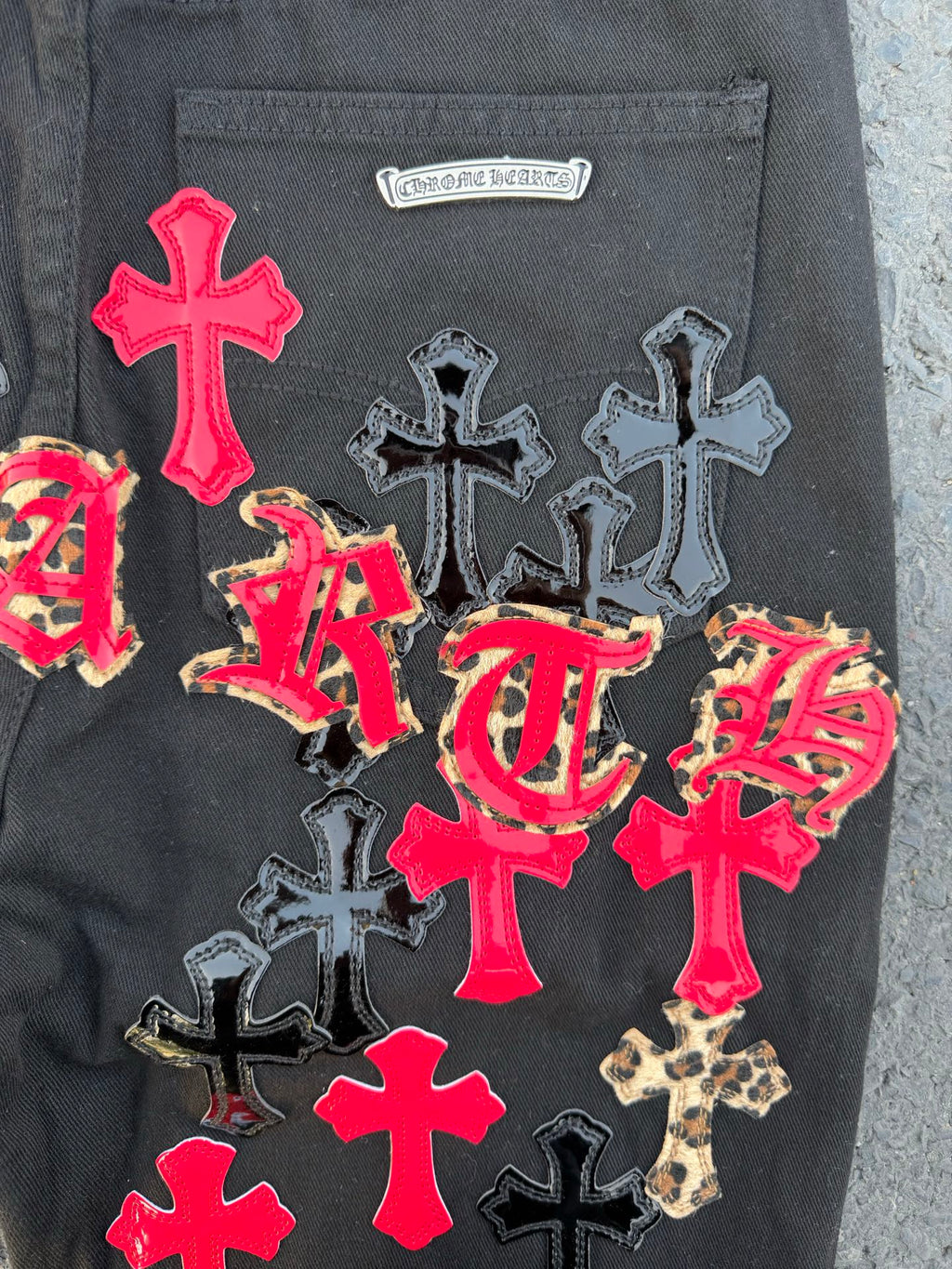 Dark gray denim pants with a small logo label and colorful cross patches.