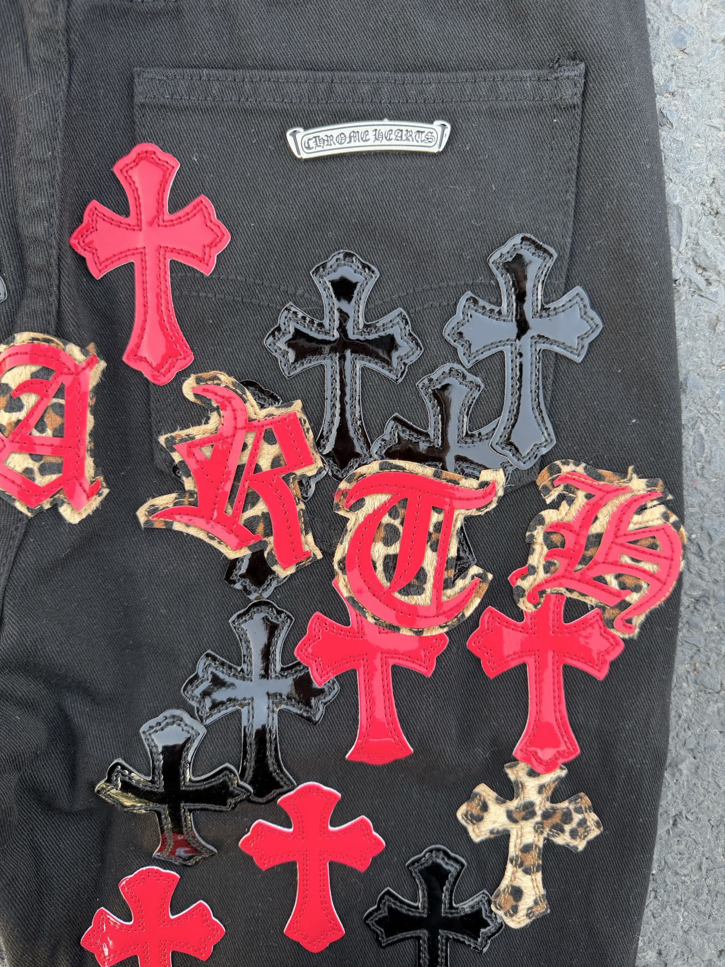 Dark gray denim pants with a small logo label and colorful cross patches.