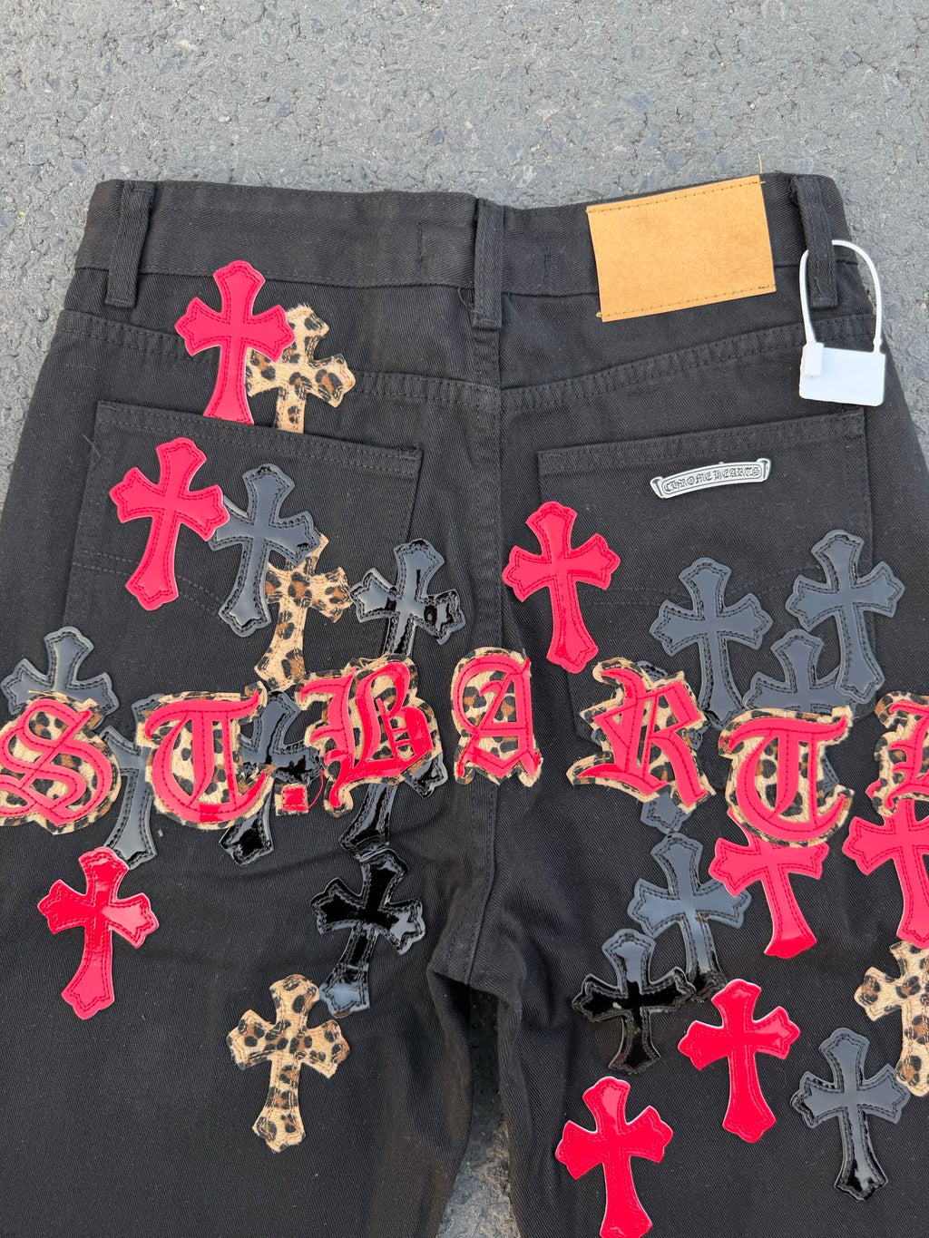 Black denim pants covered in colorful cross and script patches across the front.