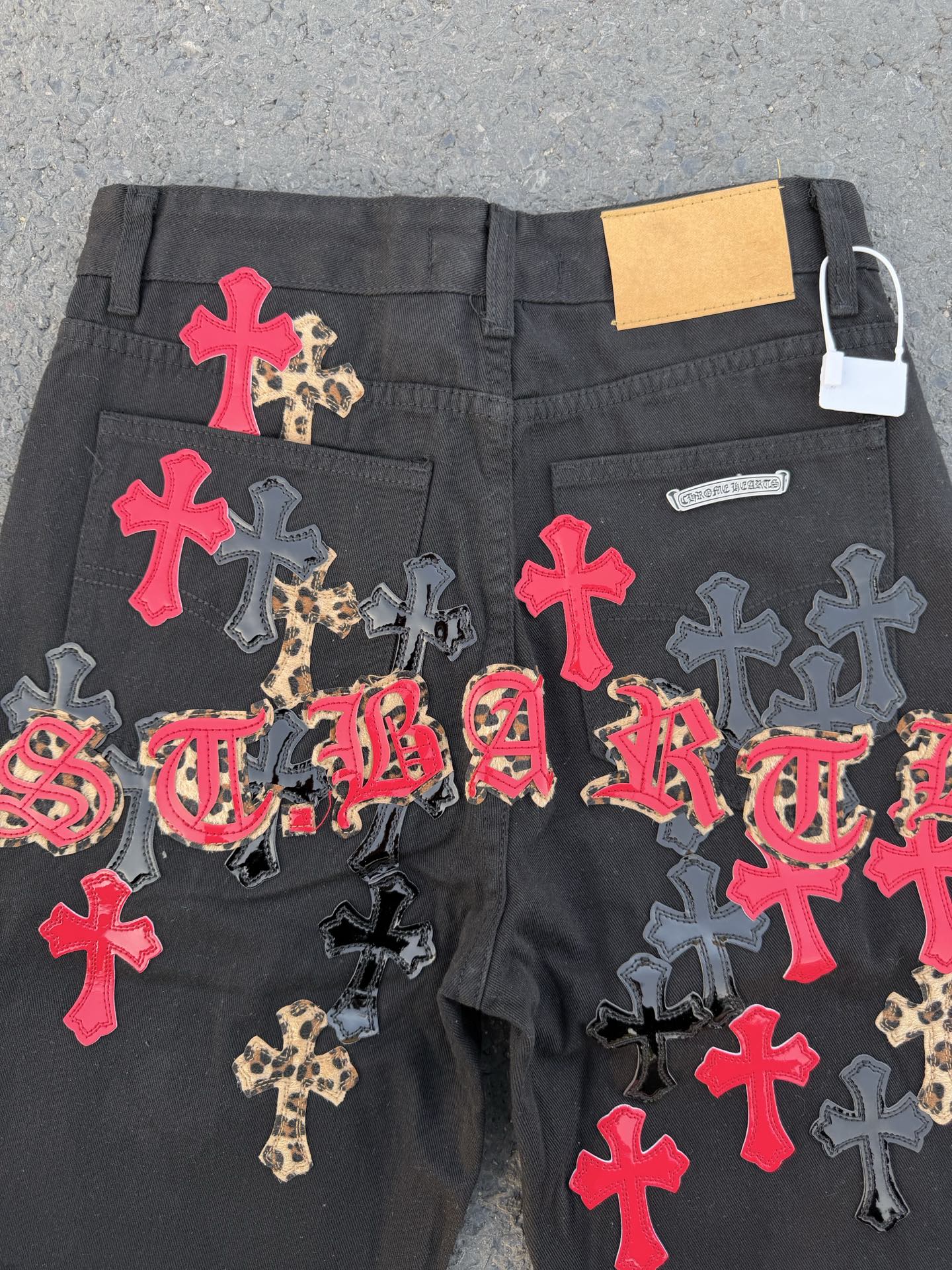Black denim pants covered in colorful cross and script patches across the front.