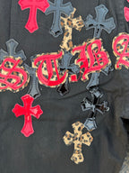 Black denim pants with colorful cross patches and script embroidery on the leg.