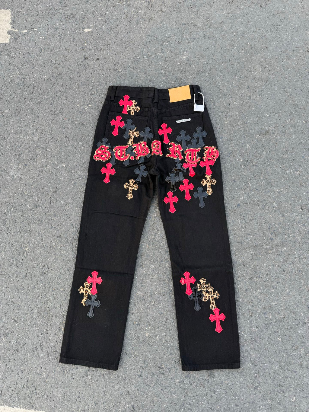 Black denim pants with colorful cross patches and a white tag on the waistband.