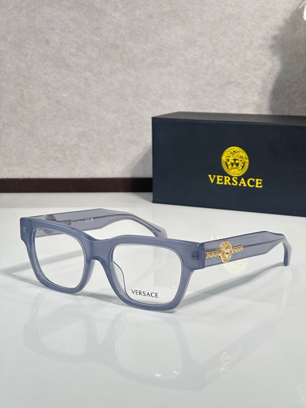 Versace eyeglasses with light blue-gray frame and gold Medusa emblem on the temple, clear lenses