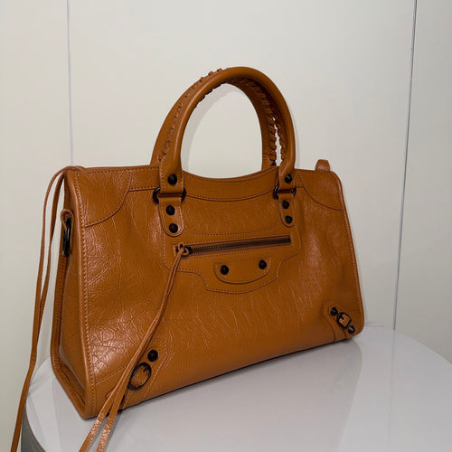 Balenciaga bag in tan leather with front zip, studs, and shoulder strap.