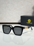Versace eyeglasses with black frames, dark lenses, gold temple badge on side.