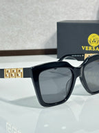 Versace eyeglasses close-up, black frames with gold geometric temple logo, dark lenses.