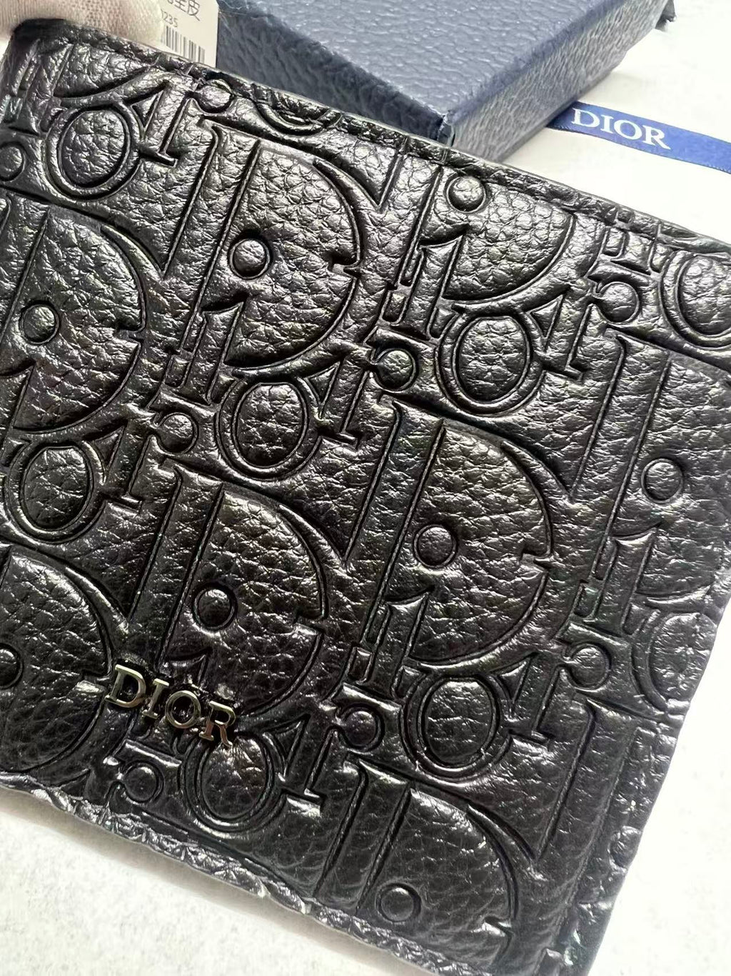 Small leather card holder close-up of Dior monogram embossing on black textured surface.