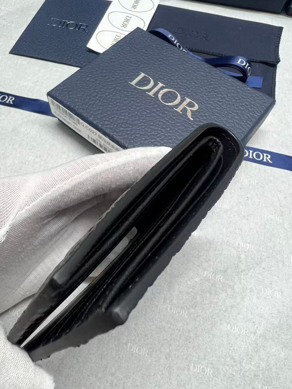 Small leather card holder with black fold and Dior branding, side view.