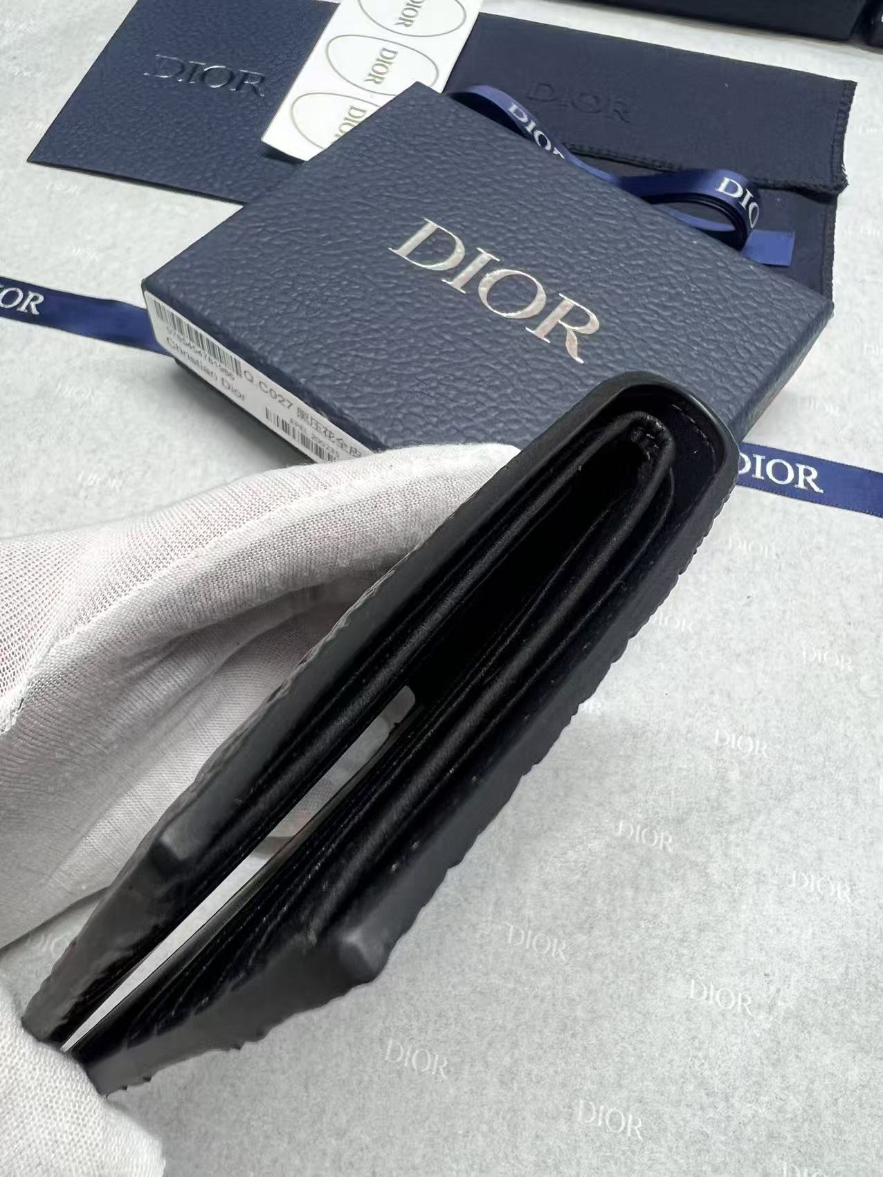 Small leather card holder with black fold and Dior branding, side view.
