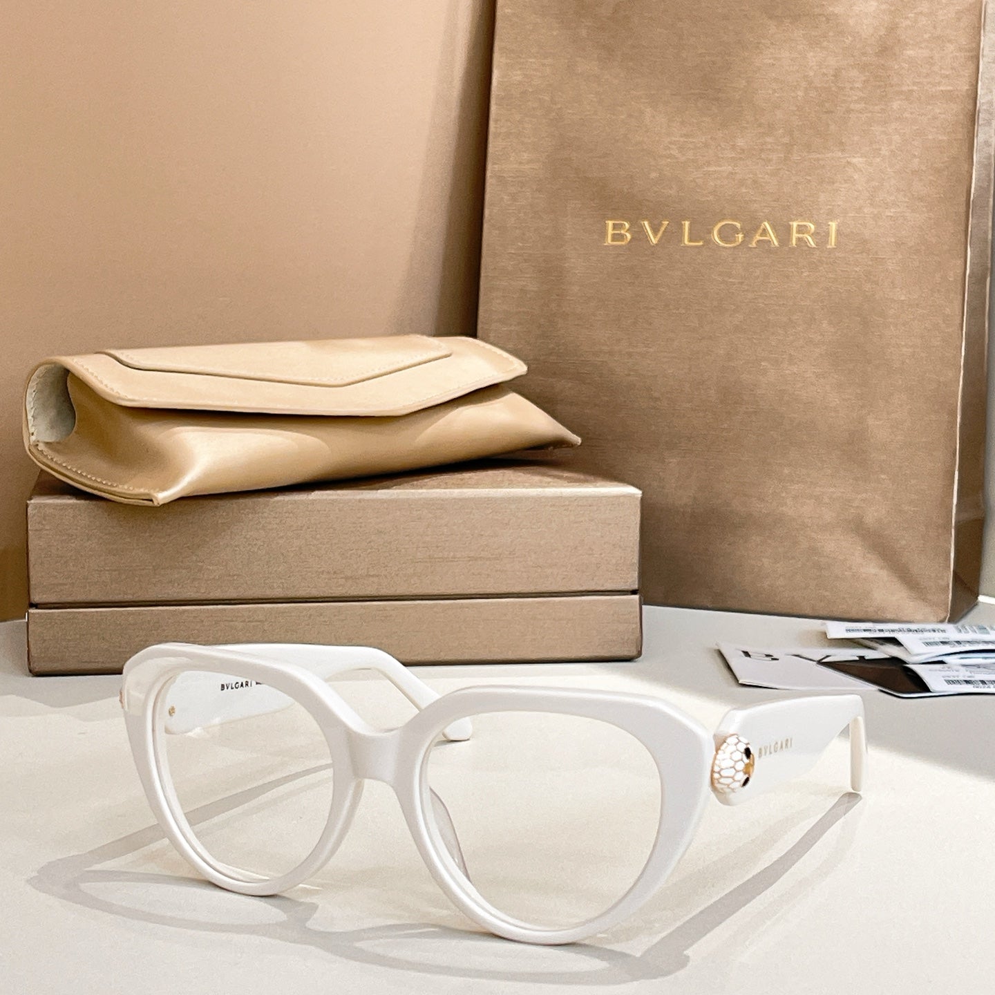 White round eyeglasses with thick frame and gold logo emblem on temple.