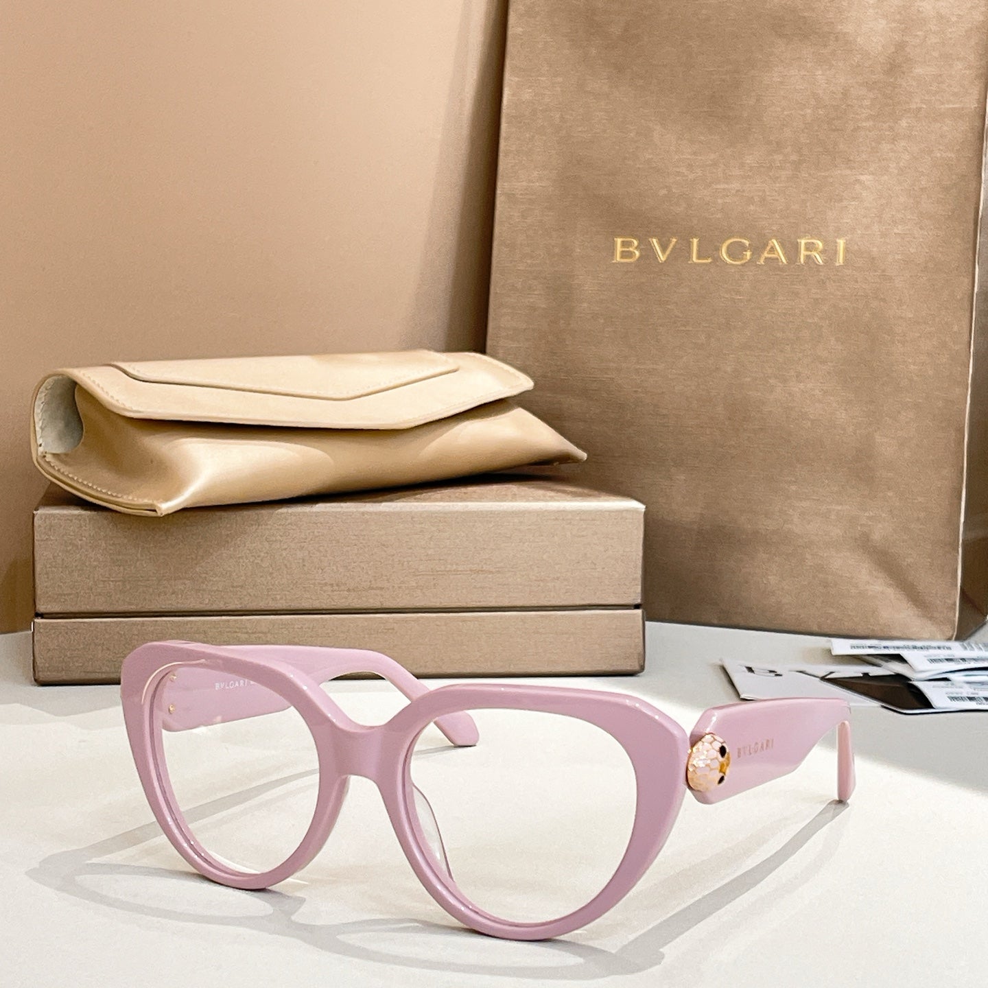 Light pink round eyeglasses with thick frame and gold logo emblem on temple.