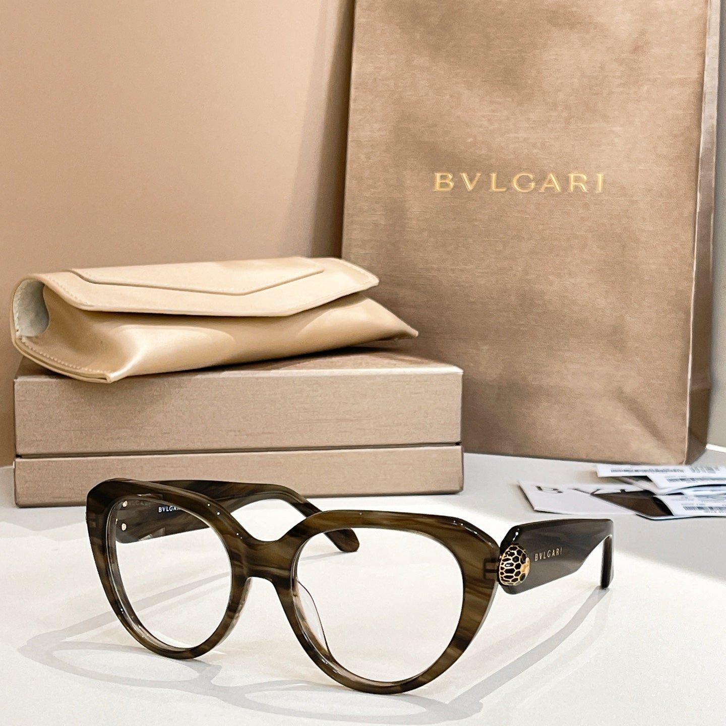 Dark tortoiseshell round eyeglasses with thick frame and gold logo emblem on temple.