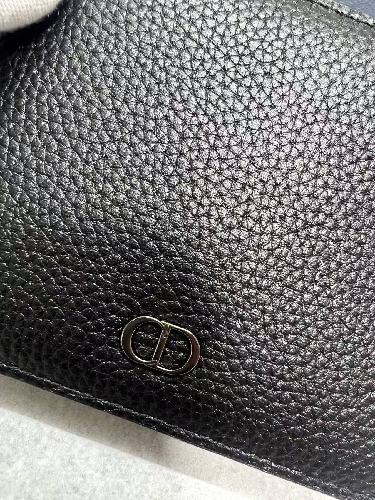 Small leather wallet, close-up of Dior metal emblem on black textured leather