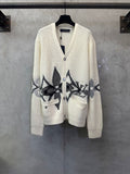 Cream knit cardigan with V-neck, button front, and black patterned chest and pocket motifs