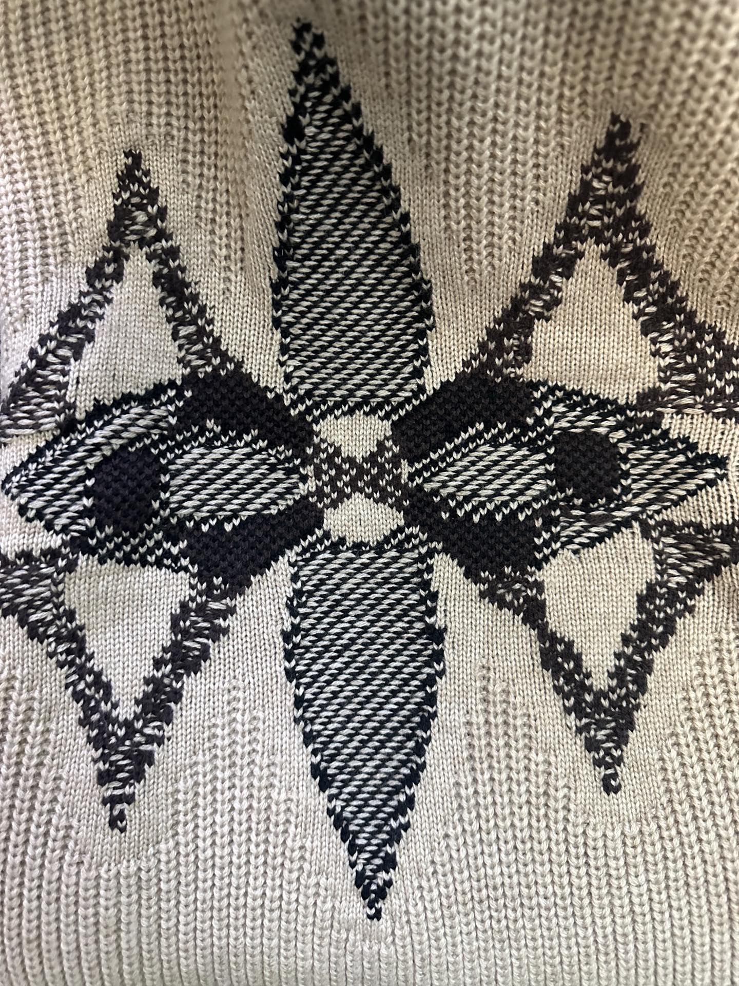 Close-up of beige knit fabric with black geometric diamond motif