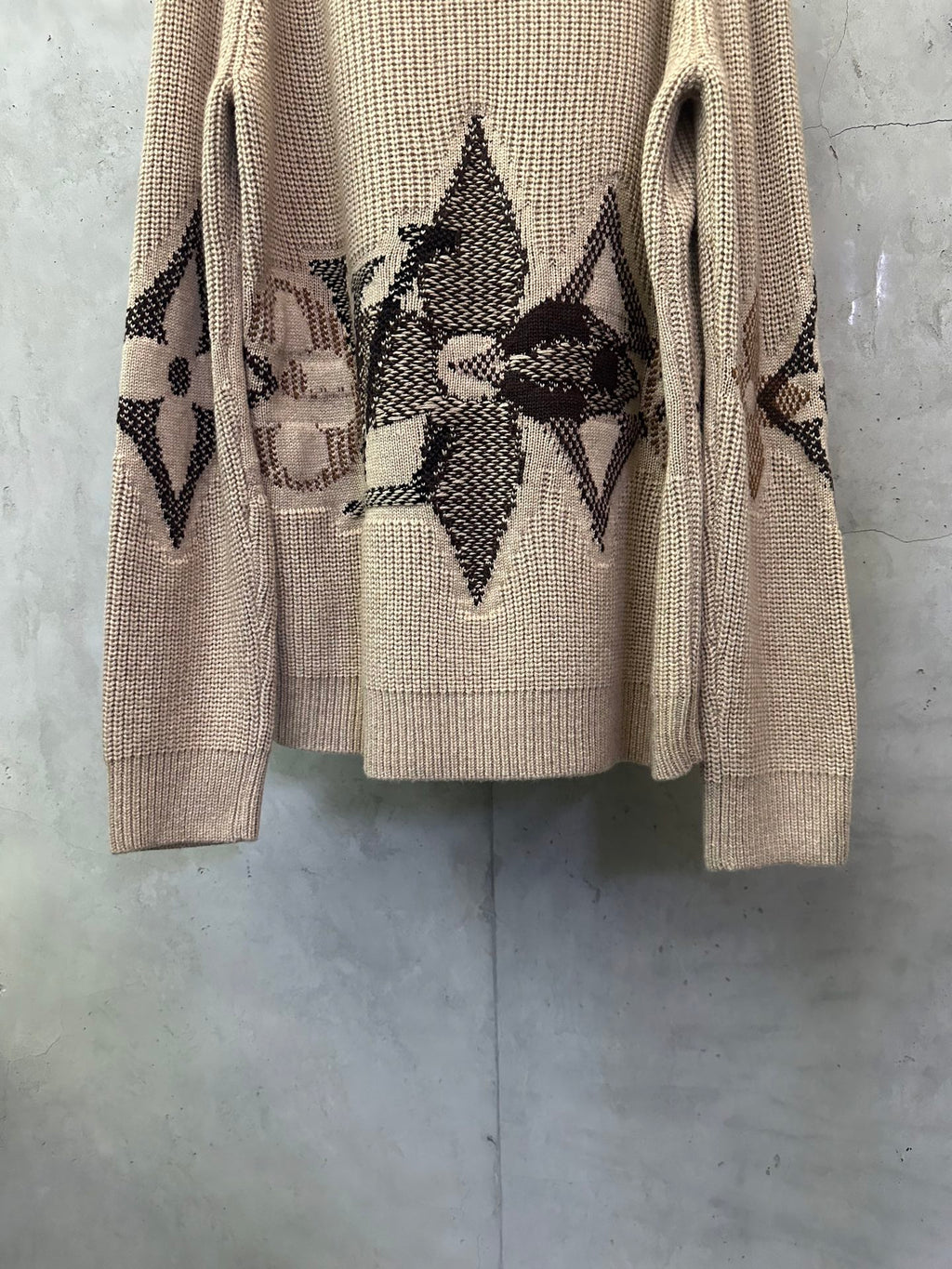 Beige knit sweater with centered black patterned motif on the lower back