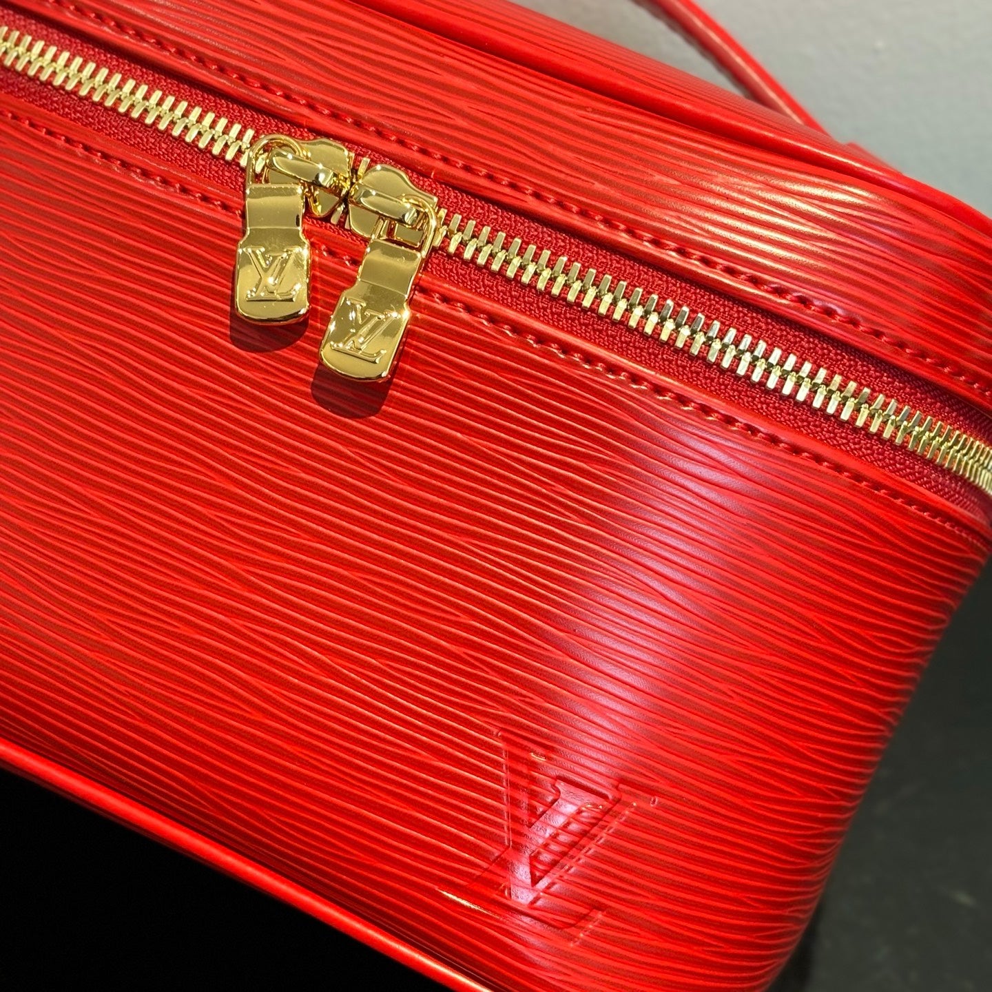 Louis Vuitton red cosmetic bag close-up: gold zipper pulls on textured leather.