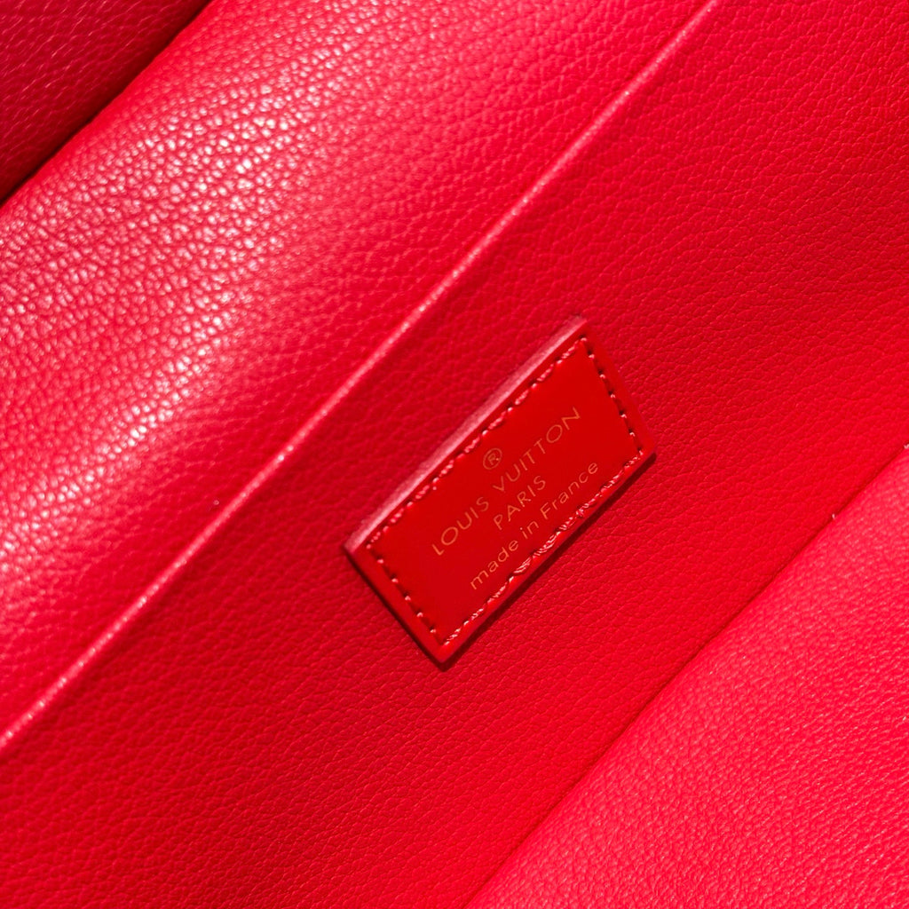 Louis Vuitton red bag close-up of leather brand patch with embossed text.
