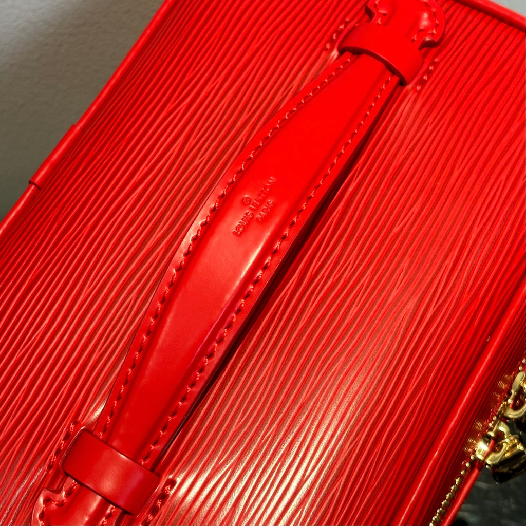 Louis Vuitton red cosmetic bag close-up of leather strap with gold hardware.