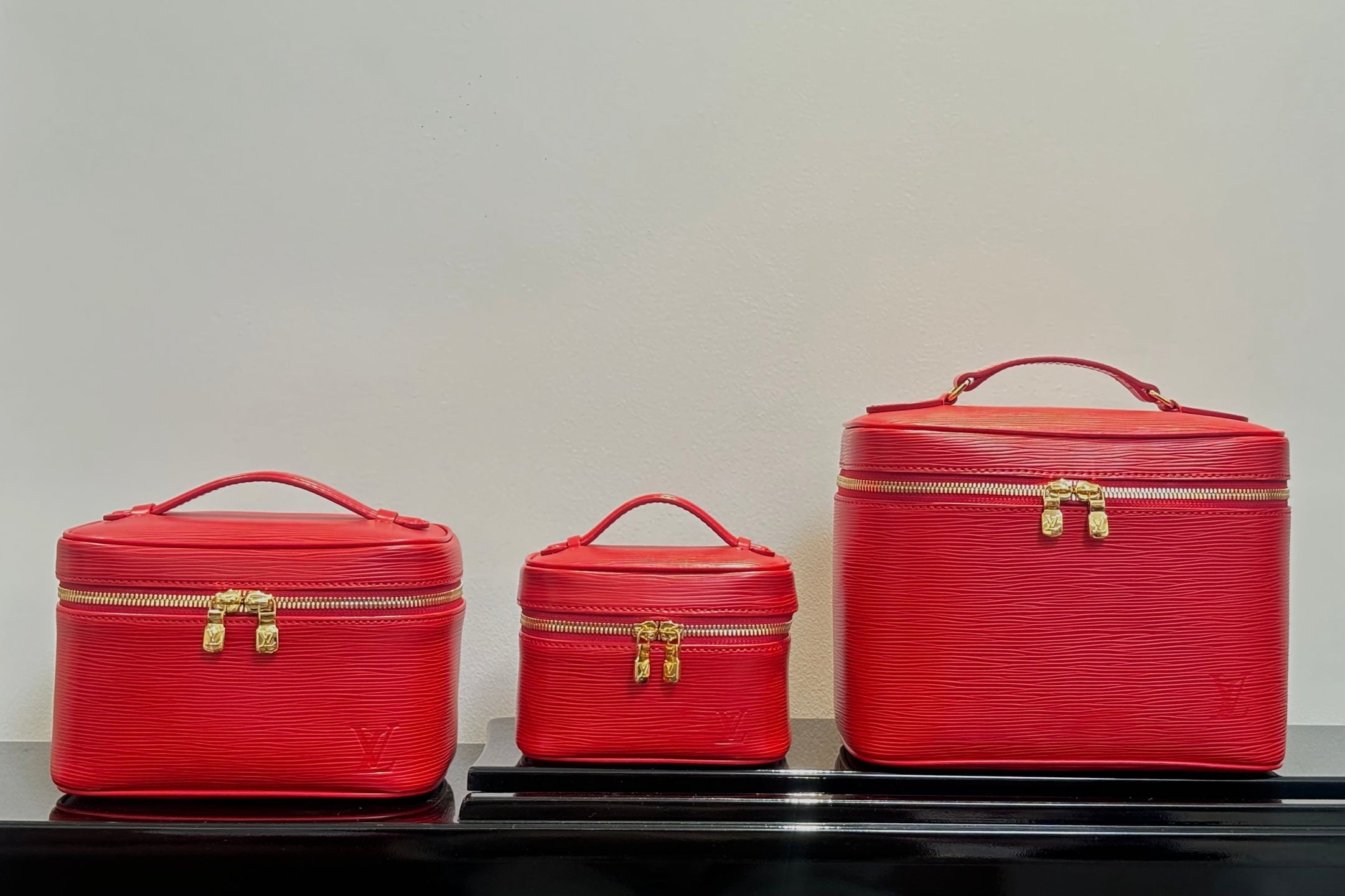Louis Vuitton red cosmetic bag set: small, medium, and large cases with handles.