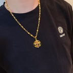 Gold-tone chain necklace with round red enamel crest pendant on dark T-shirt neckline.