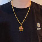 Gold-tone chain necklace with round red enamel crest pendant worn on dark T-shirt.