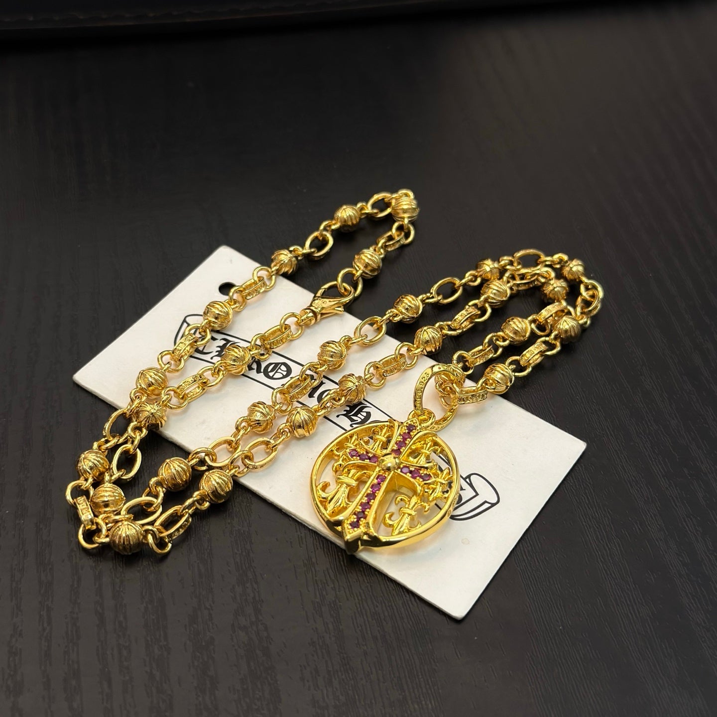 Gold-tone chain necklace with round red enamel crest pendant, layered on cards.