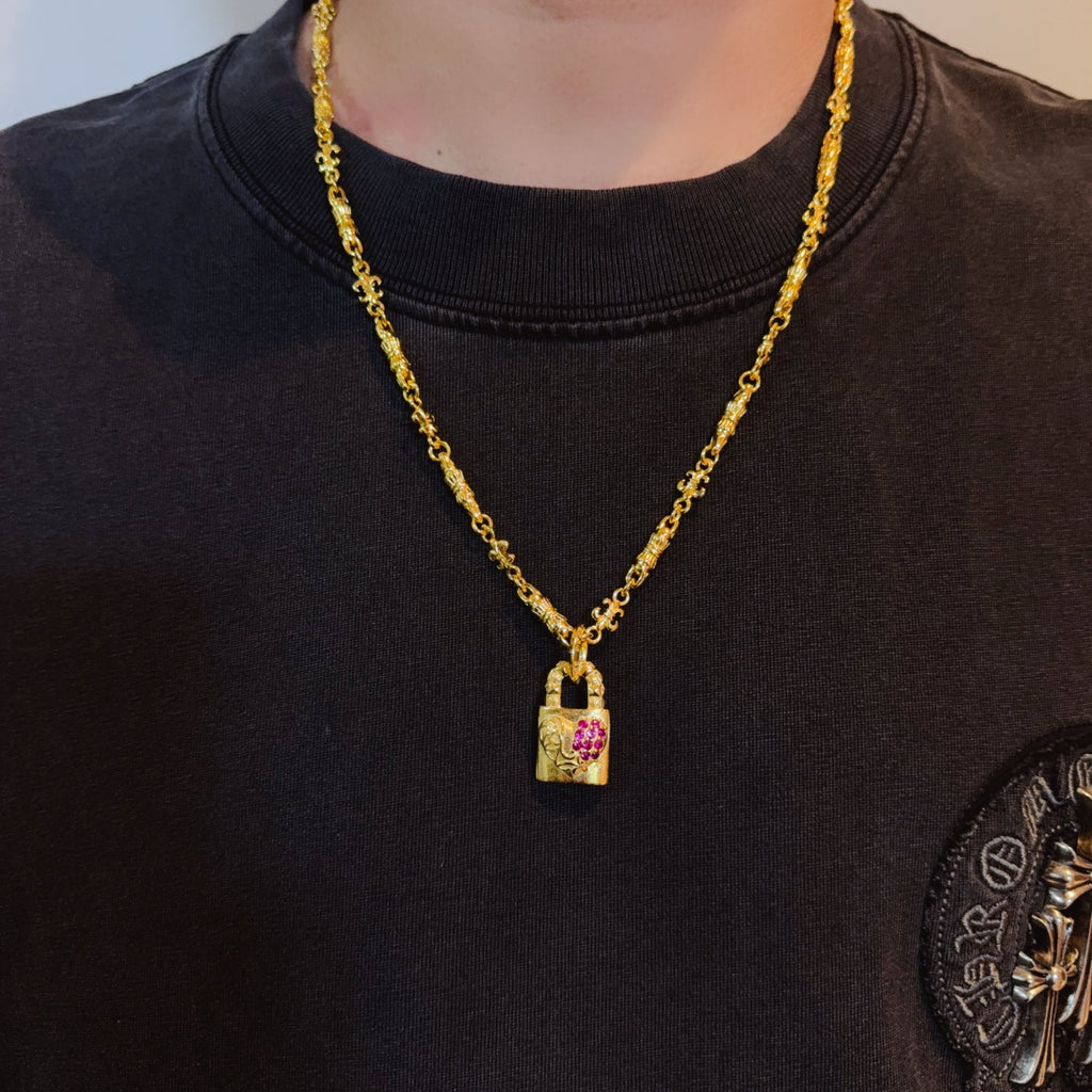 Gold-tone pendant necklace worn on a black shirt; rectangular pink gemstone charm