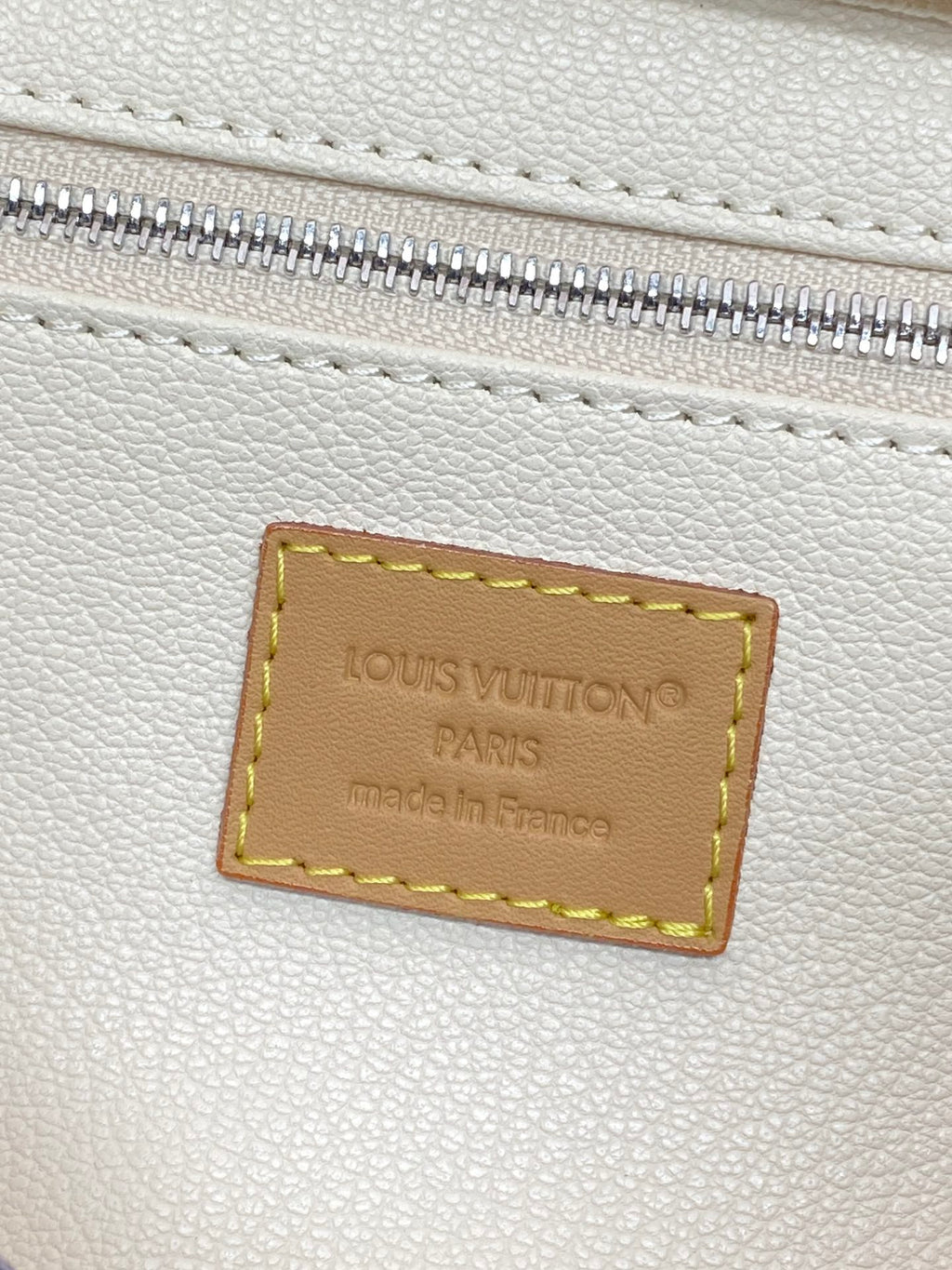 Cream leather patch label inside zipper opening with stitched border and engraved text.