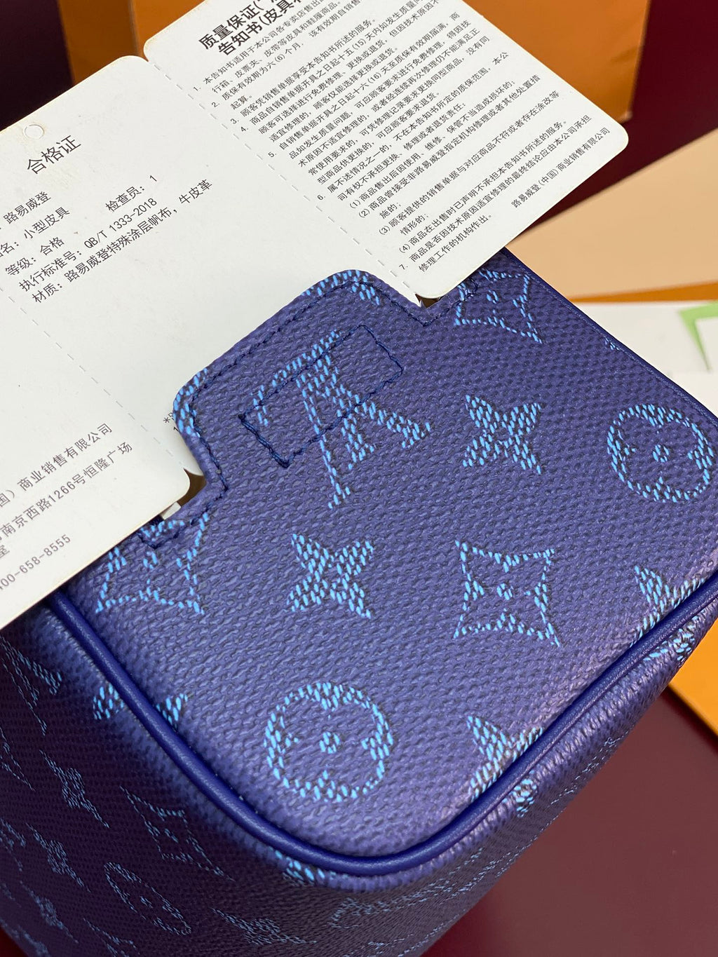 Blue monogram bag top close-up with embossed pattern and curved zip pocket edge.
