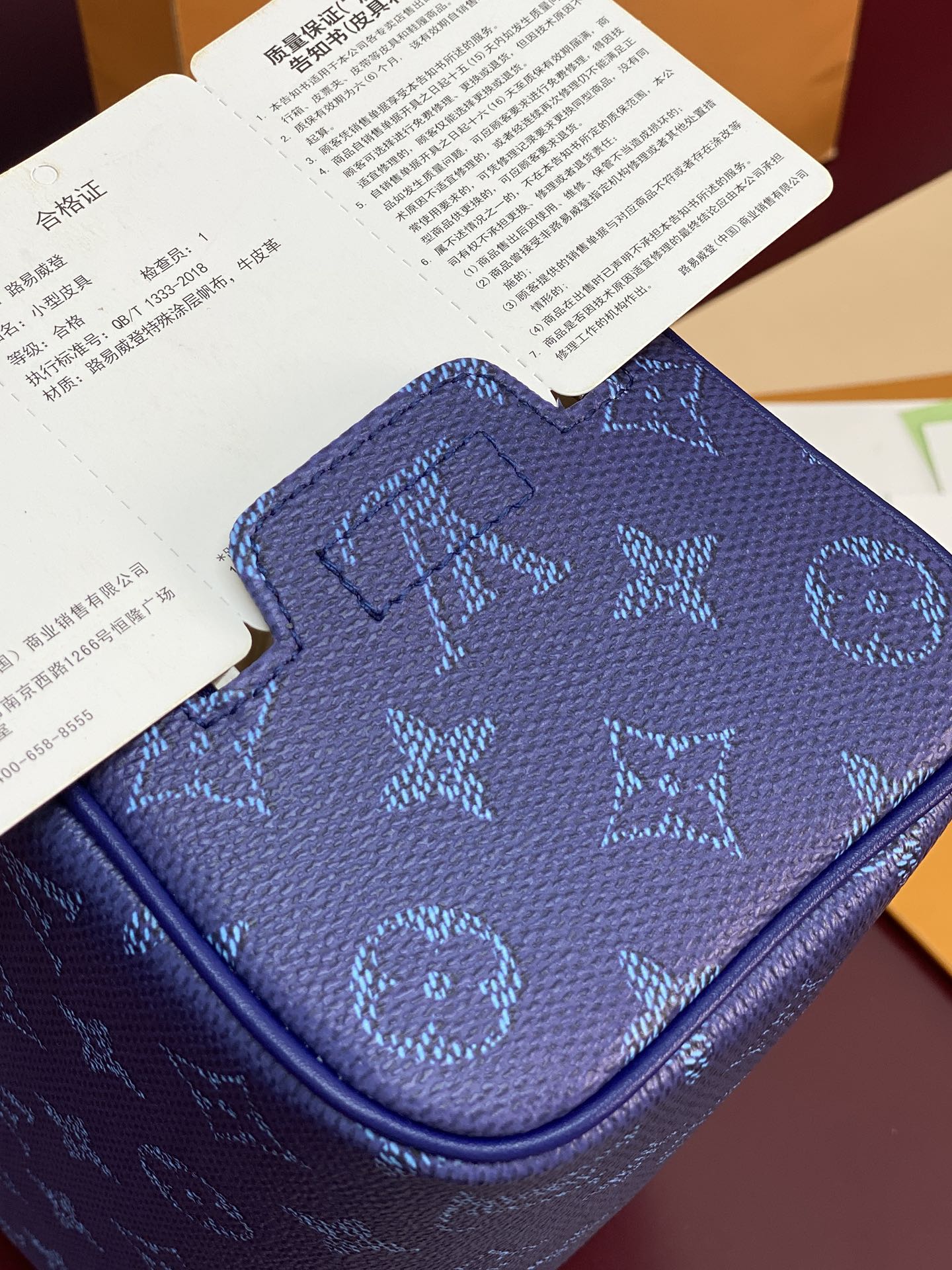Blue monogram bag top close-up with embossed pattern and curved zip pocket edge.