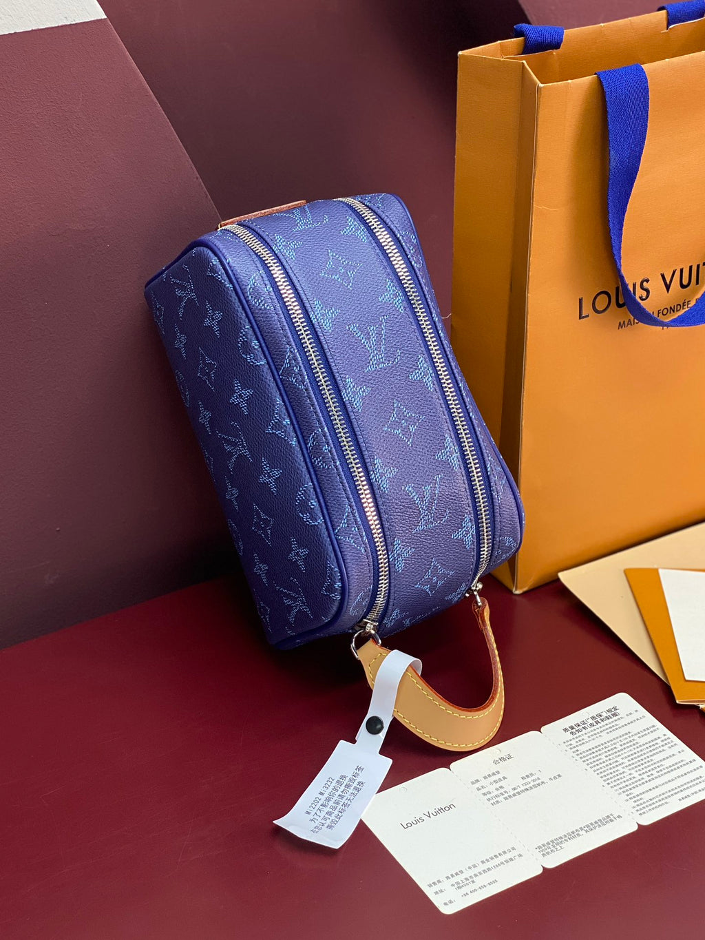 Blue monogram crossbody bag with rounded top zip and tan leather strap and tag.