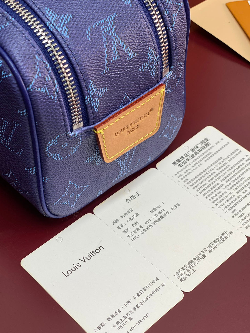 Blue monogram bag front with tan leather logo patch and gold-tone zipper edge.