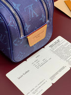 Blue monogram bag front with tan leather logo patch and gold-tone zipper edge.