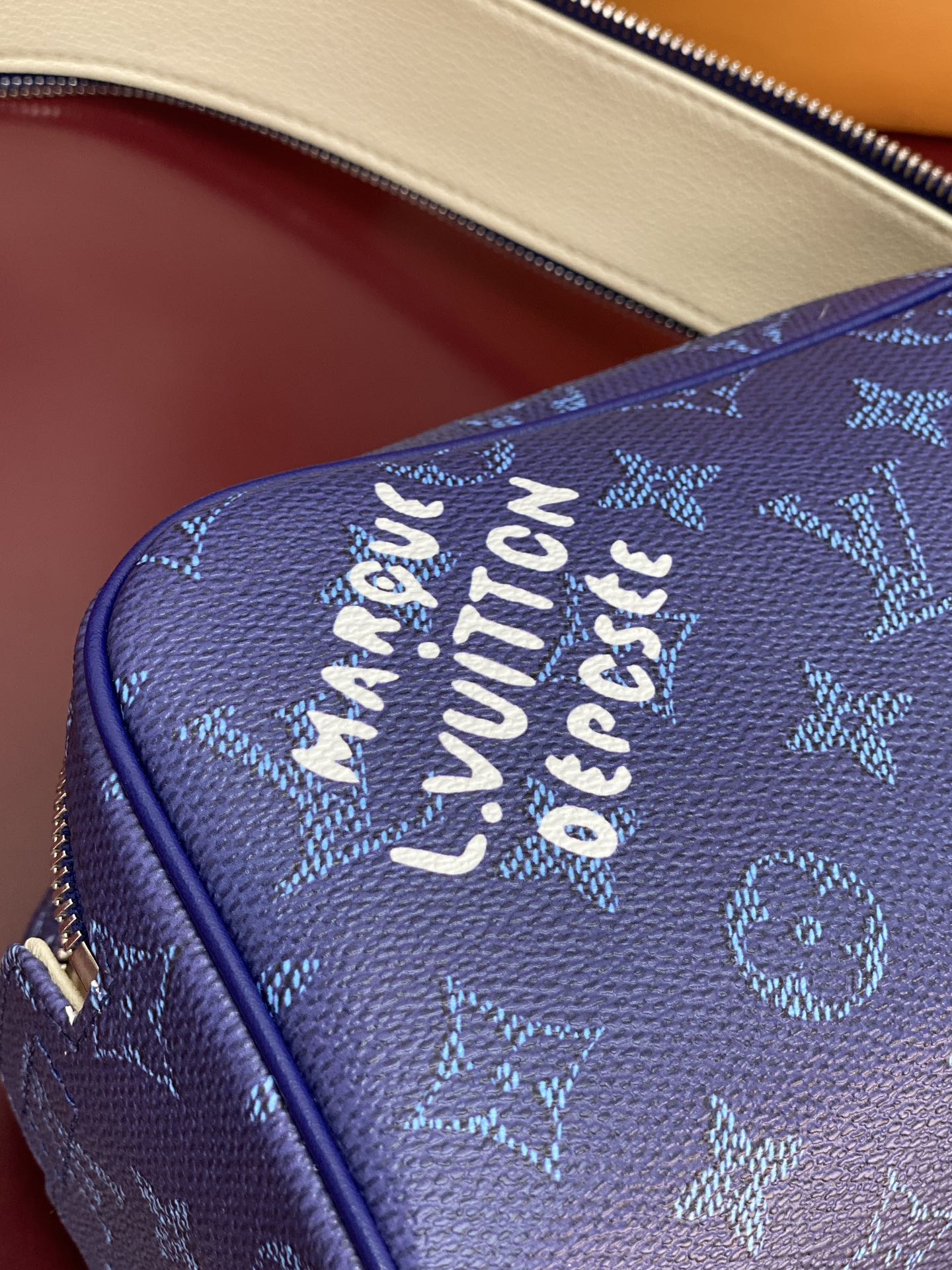 Blue monogram bag side close-up with embossed lettering and gold-tone zipper trim.
